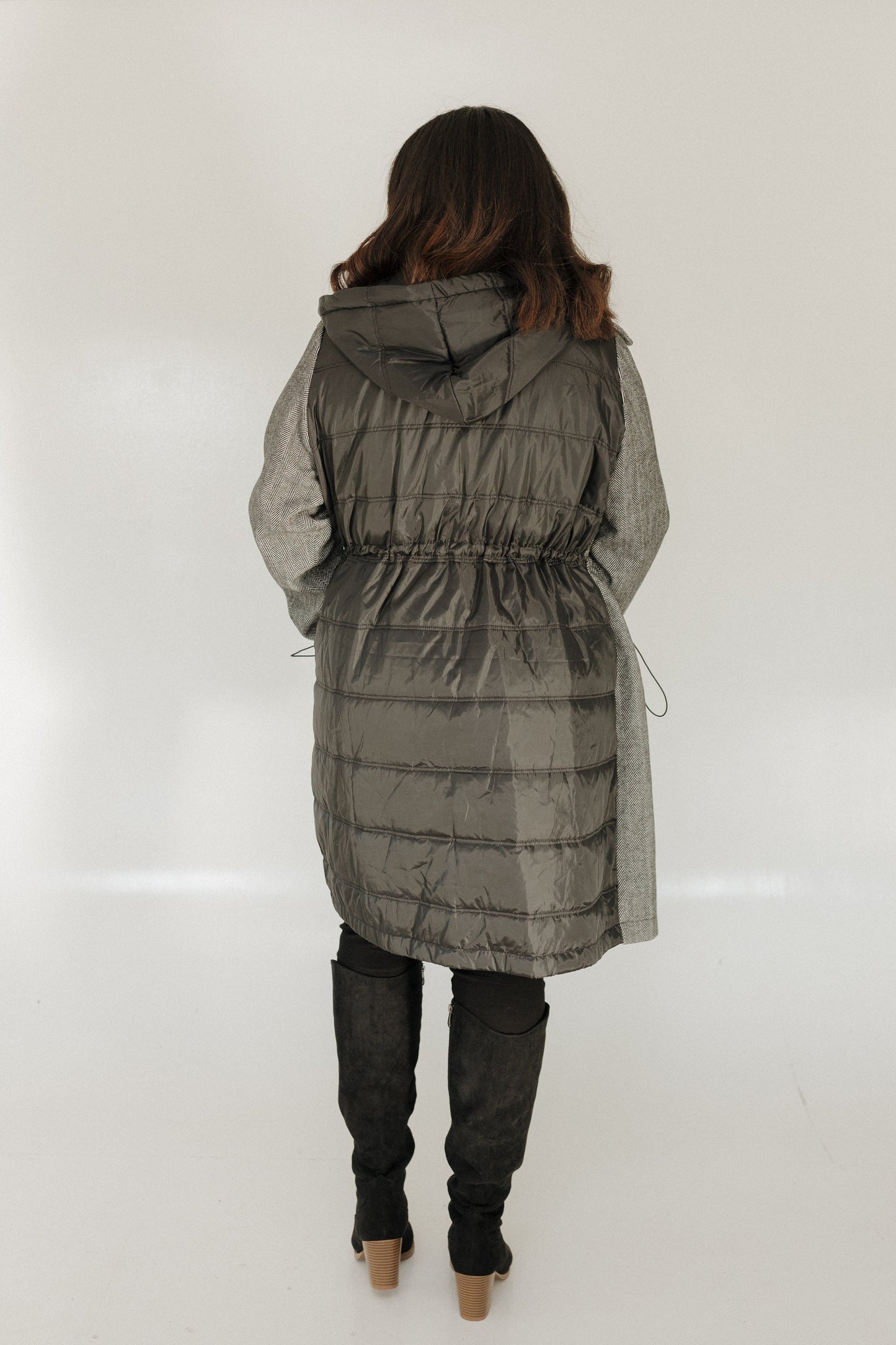 Person wearing a long gray quilted coat on a white background
