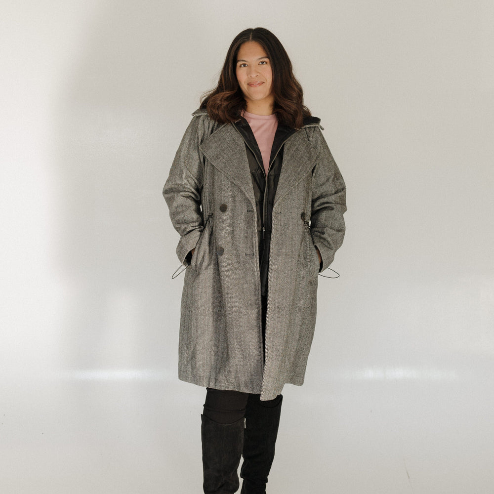 Person wearing a long gray coat against a white background