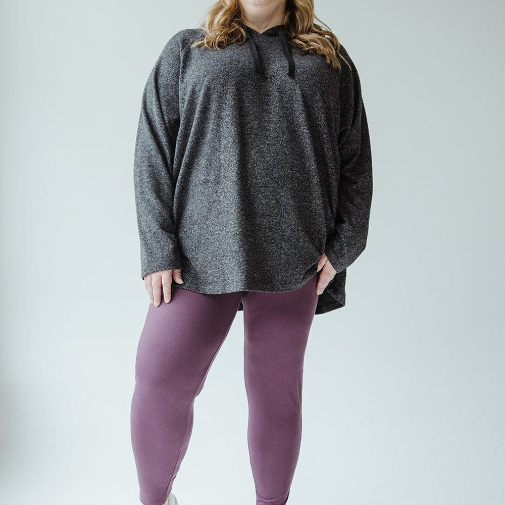 A person with long hair wearing a gray hoodie, Zenana High-Waisted Super Soft Leggings in Antique Violet, and white sneakers smiles while standing against a plain background.