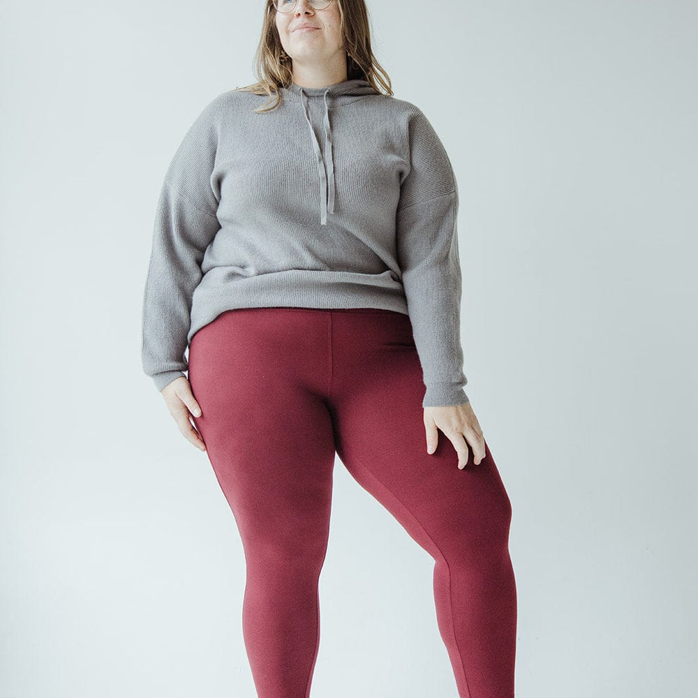 A person stands against a plain background, wearing a grey sweatshirt, HIGH-WAISTED SUPER SOFT LEGGINGS IN DEEP BURGUNDY by Zenana, and black shoes.