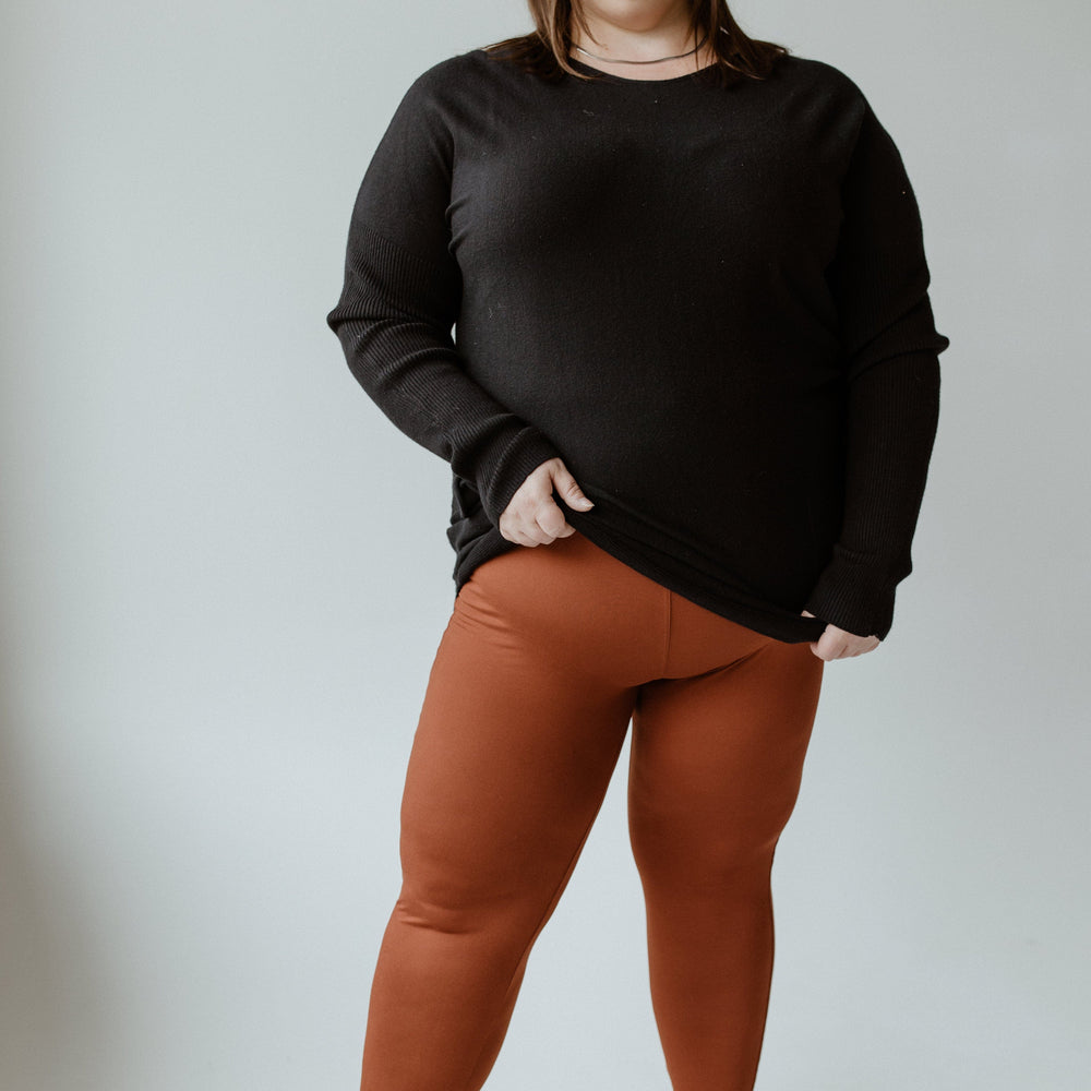 A woman stands against a plain background, wearing a black sweater and ultra-soft, high-waisted leggings paired with black sneakers.