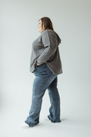 A person wearing a gray sweater and Judy Blue high-waisted button-fly destroyed hem straight leg jeans stands in profile against a light background.