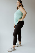 A person in a mint green tank top, Zenana's HIGH-WAISTED SUPER SOFT LEGGINGS IN BLACK, and white sneakers stands with hands on hips against a plain background.