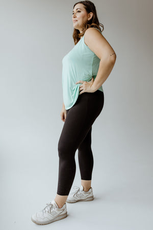 A woman in a green tank top and Zenana's high-waisted super soft leggings in black stands in profile, looking forward.