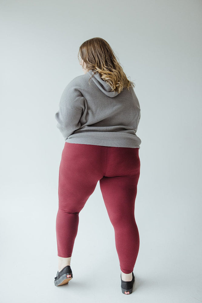 Person in a grey hoodie and Zenana HIGH-WAISTED SUPER SOFT LEGGINGS IN DEEP BURGUNDY stands facing away from the camera against a plain background.