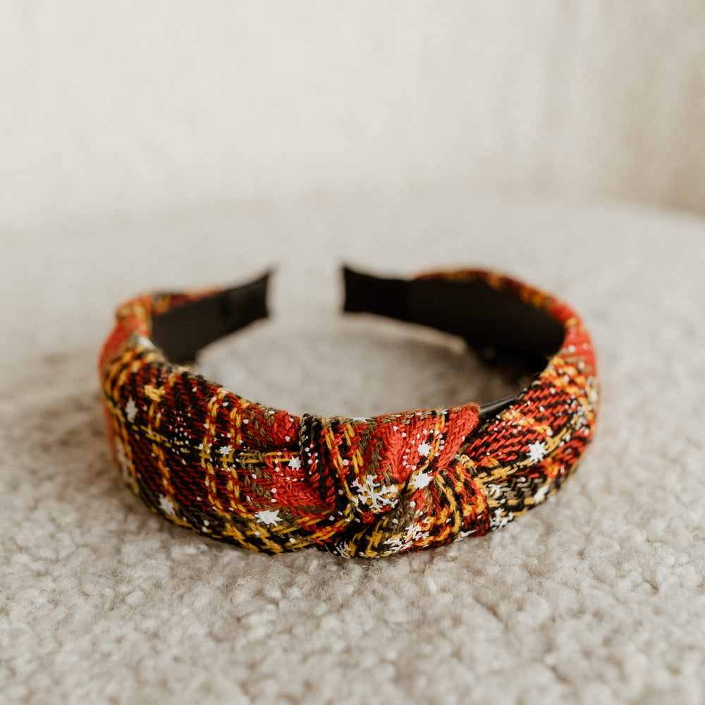 A colorful, plaid-design headband with a knot adds a festive touch as it rests on a textured, beige surface.