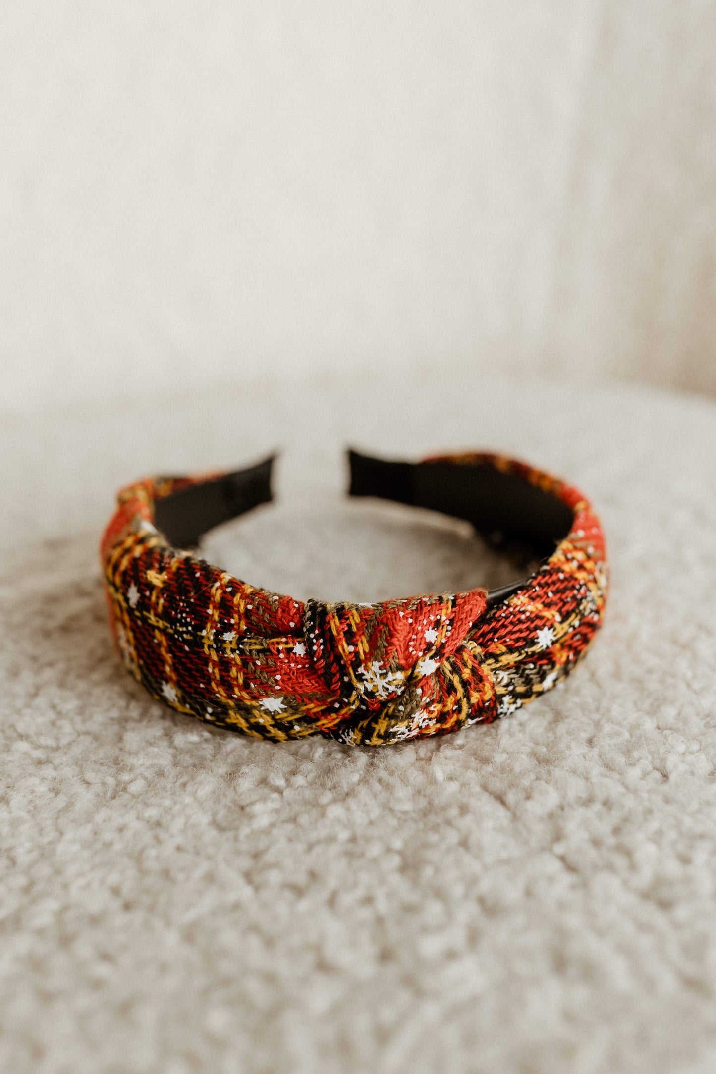 A colorful, plaid-design headband with a knot adds a festive touch as it rests on a textured, beige surface.