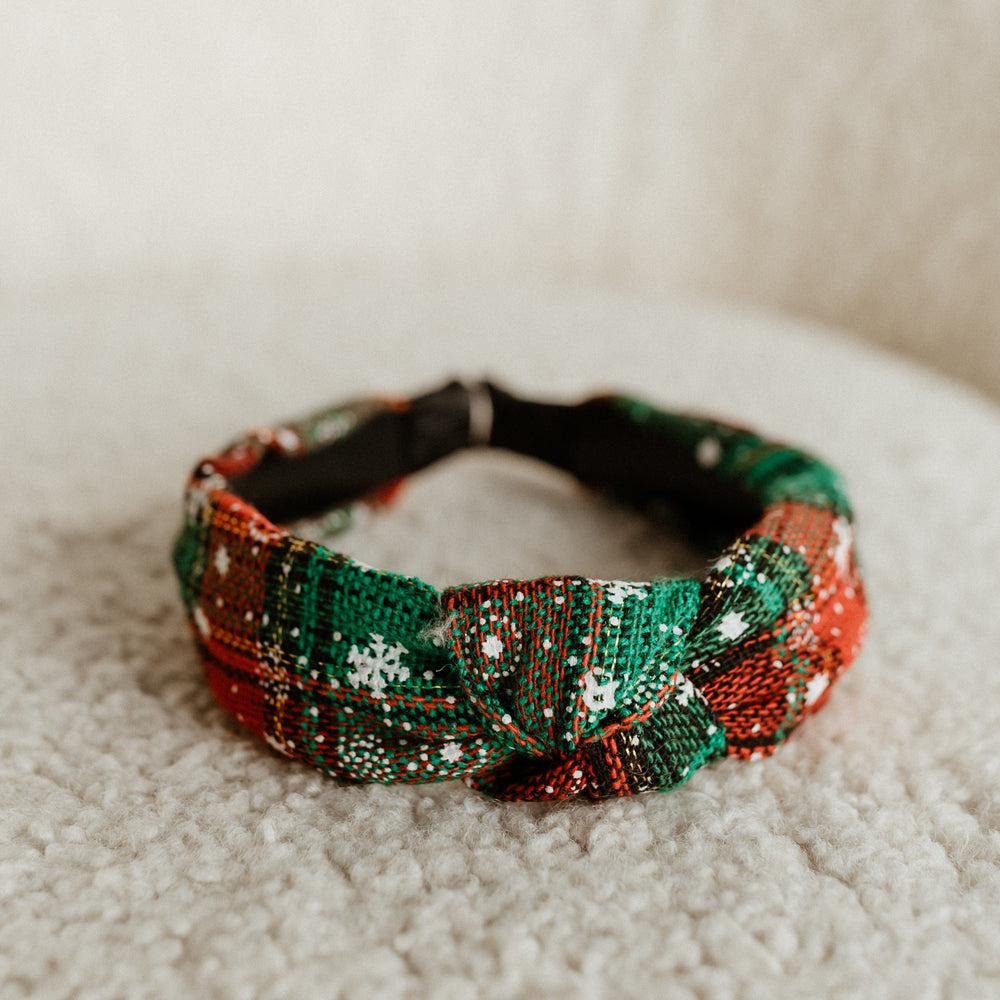 Festive plaid woven headband with red, green, and white patterns, resting on a textured white surface.