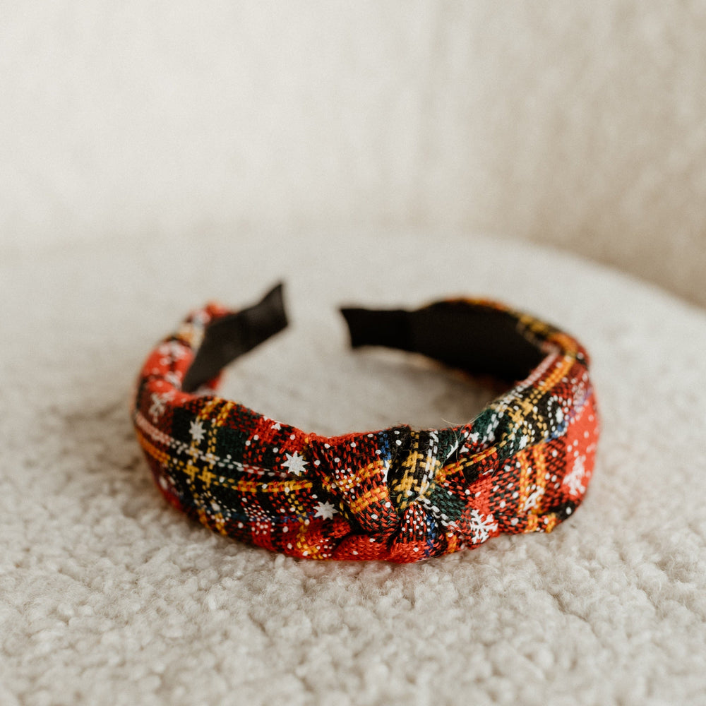 A vibrant rose plaid headband with a knot design adds festive flair, resting elegantly on a textured beige surface.