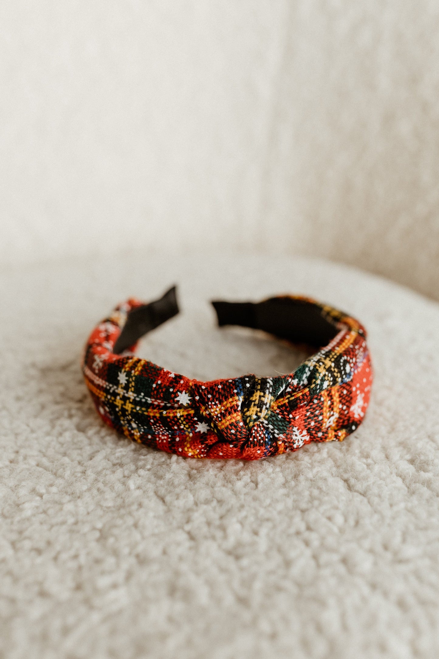 A vibrant rose plaid headband with a knot design adds festive flair, resting elegantly on a textured beige surface.