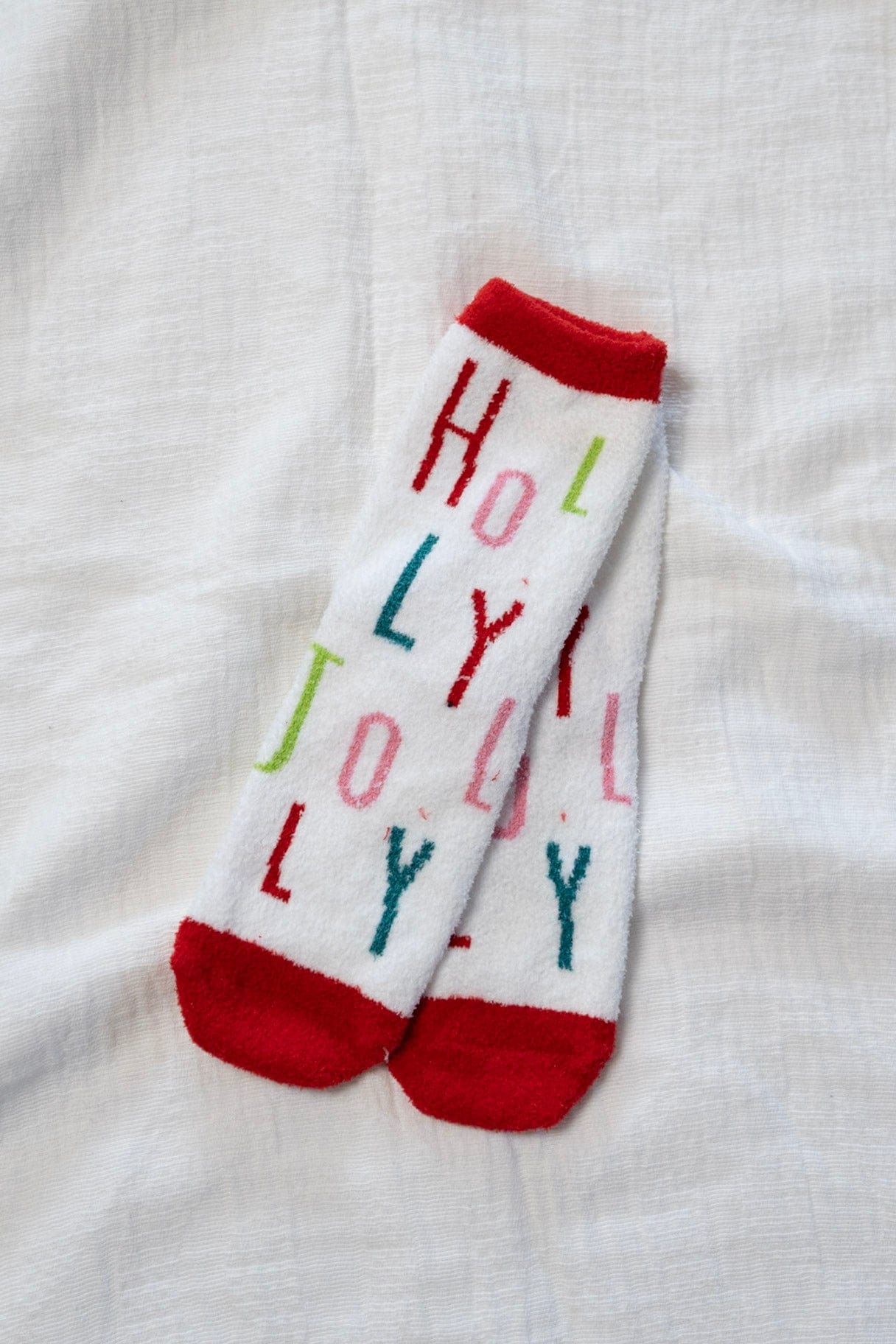 White socks with colorful text 'HOLLY JOLLY' on a white fabric background