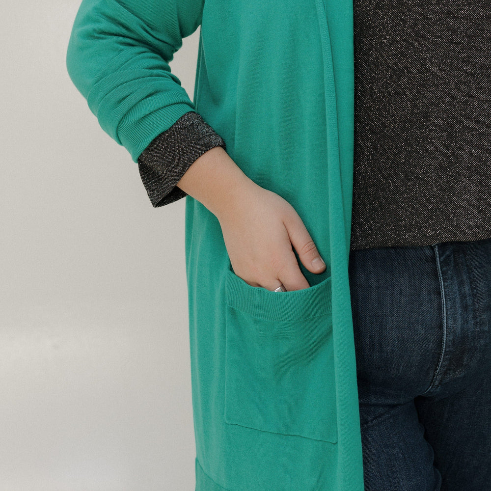 Person wearing a teal cardigan over a dark shirt with a neutral background