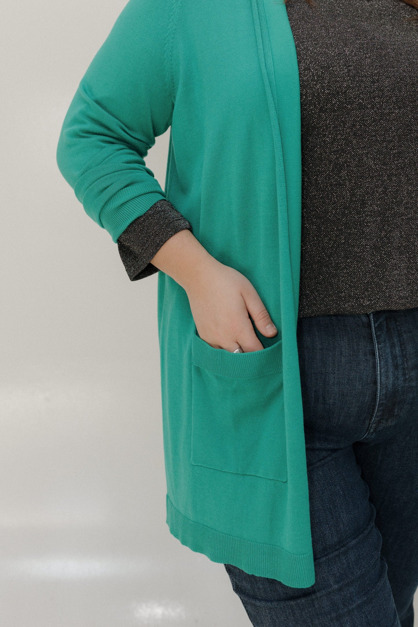 Person wearing a teal cardigan over a dark shirt with a neutral background