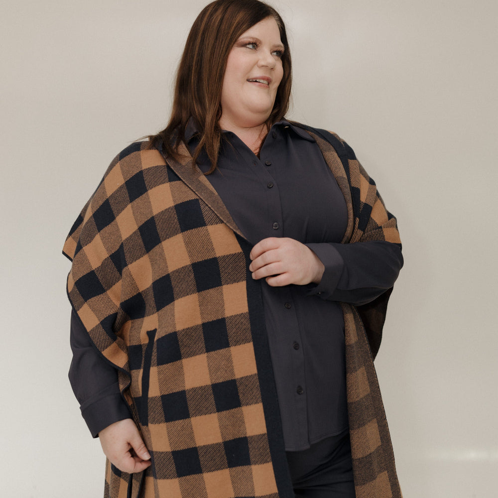 Person wearing a plaid coat over a dark shirt against a plain background