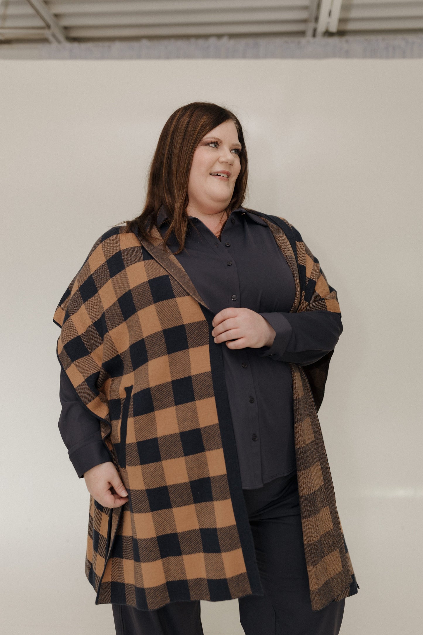 Person wearing a plaid coat over a dark shirt against a plain background