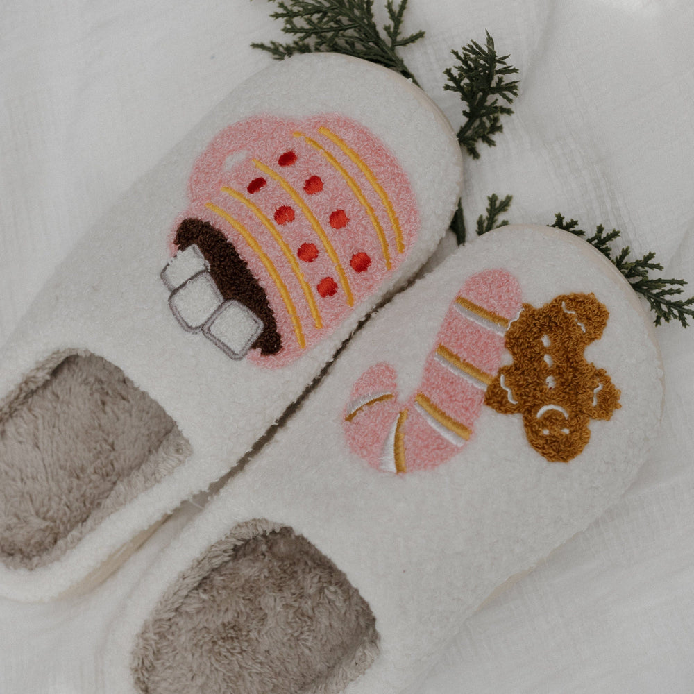 Pair of cartoon-themed slippers with a gingerbread house and bear design on a white background.