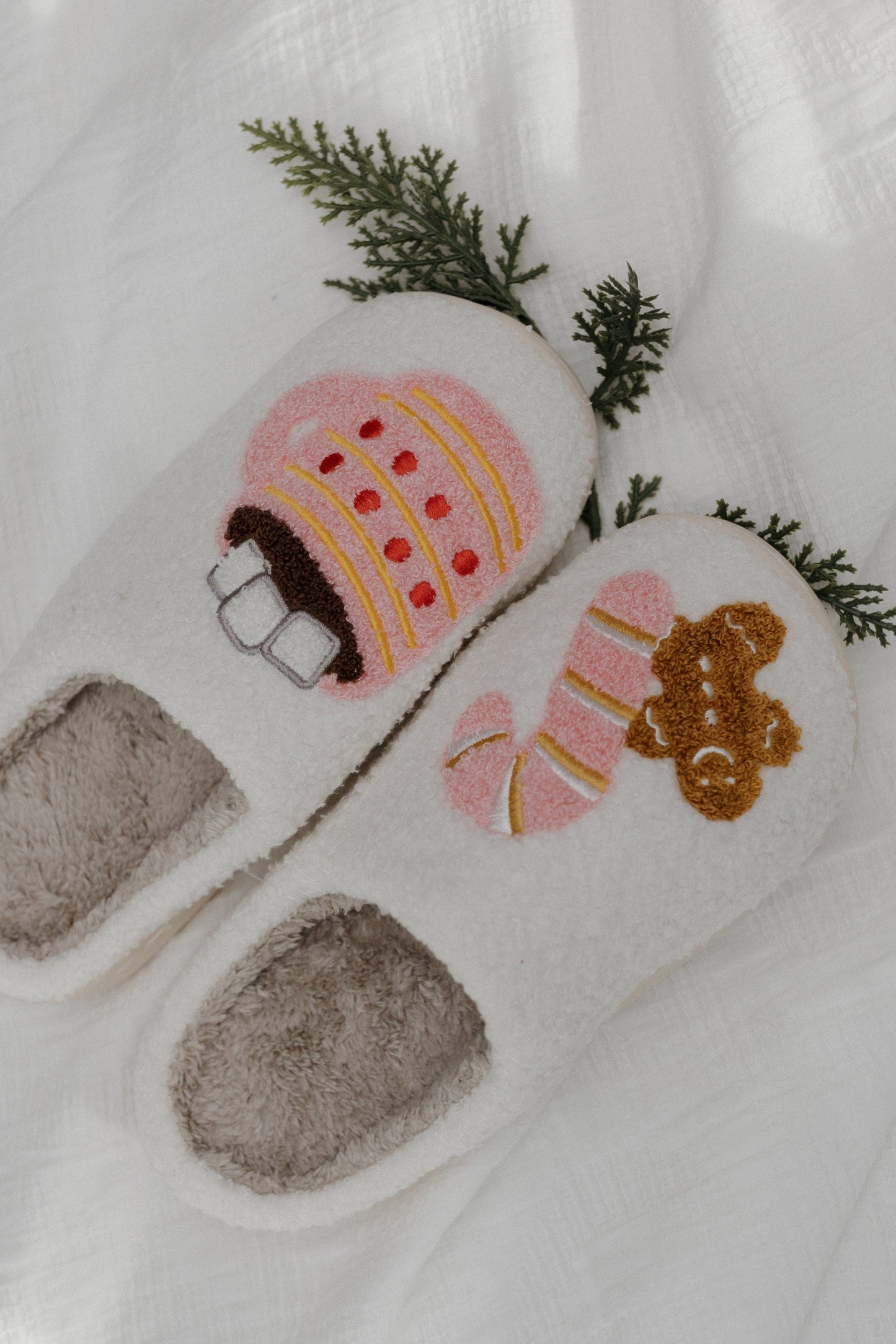 Pair of cartoon-themed slippers with a gingerbread house and bear design on a white background.