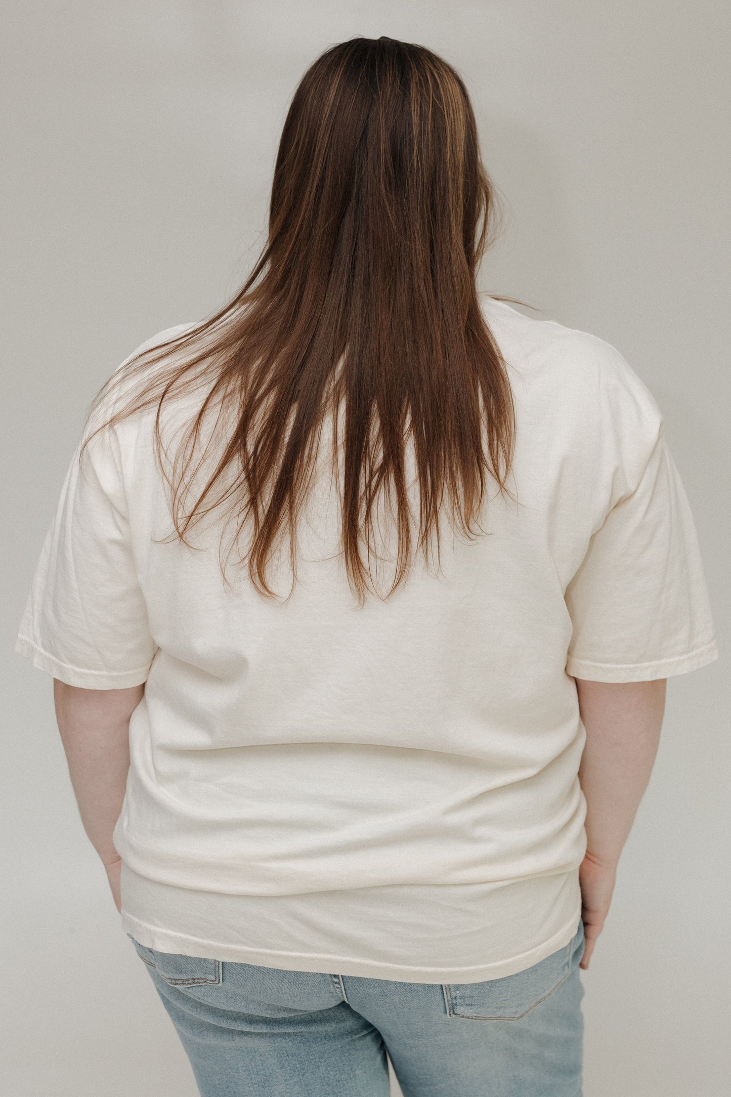 Person wearing a plain white t-shirt and light blue jeans against a neutral background