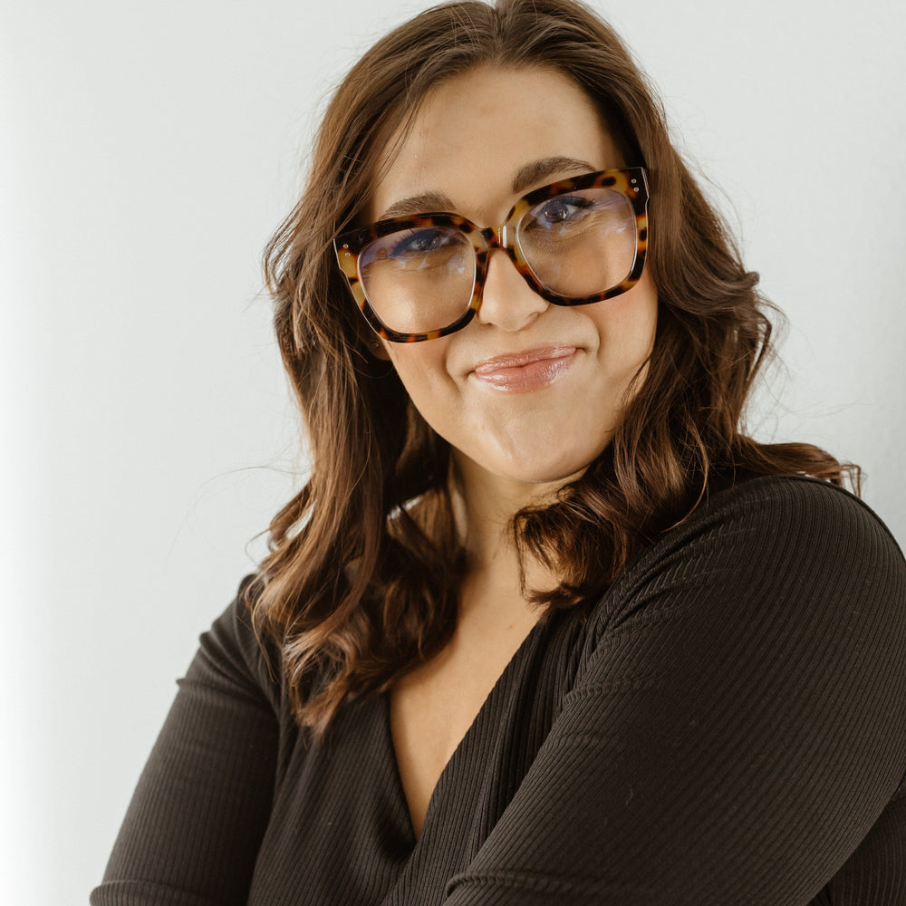 Woman wearing glasses and a dark top against a light background