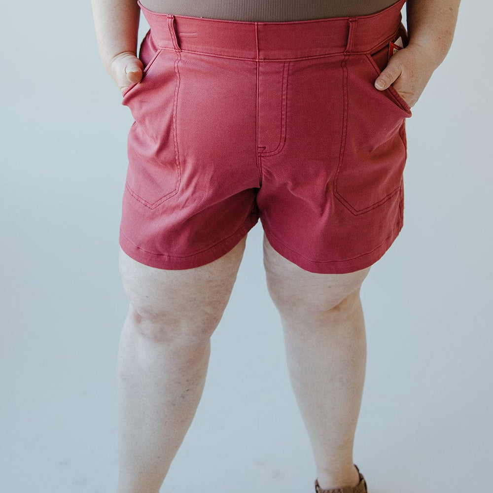 Person wearing a buttery-soft twill fabric sleeveless brown top, Spanx® STRETCH TWILL SHORTS 6" IN WILD ROSE, and sandals stands with their hands in their pockets against a plain background.