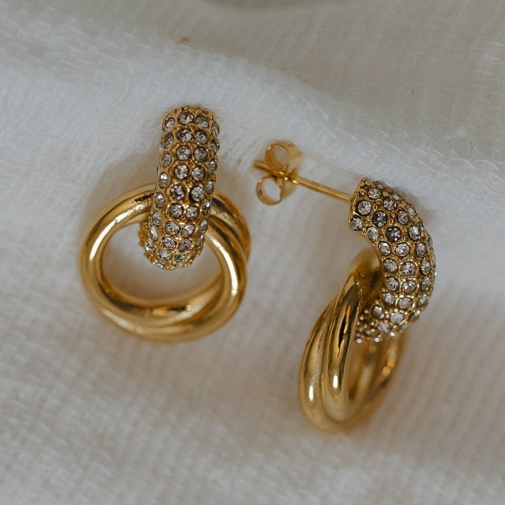 Gold hoop earrings with diamond accents on a white fabric background