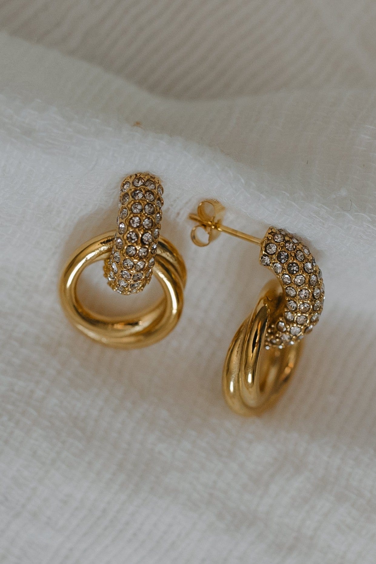 Gold hoop earrings with diamond accents on a white fabric background
