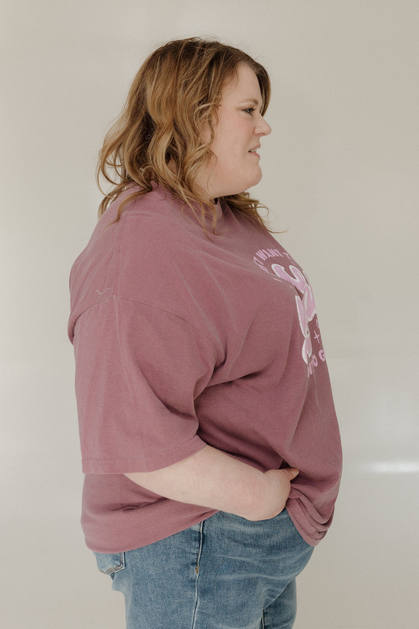Person wearing a berry oversized sweatshirt with text on it against a plain background