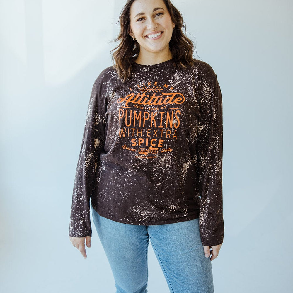 A person smiles while wearing Love Marlow's hand-bleached "I LIKE MY ATTITUDE HOW I LIKE MY PUMPKINS WITH EXTRA SPICE" long-sleeve tee and light blue jeans against a light background.