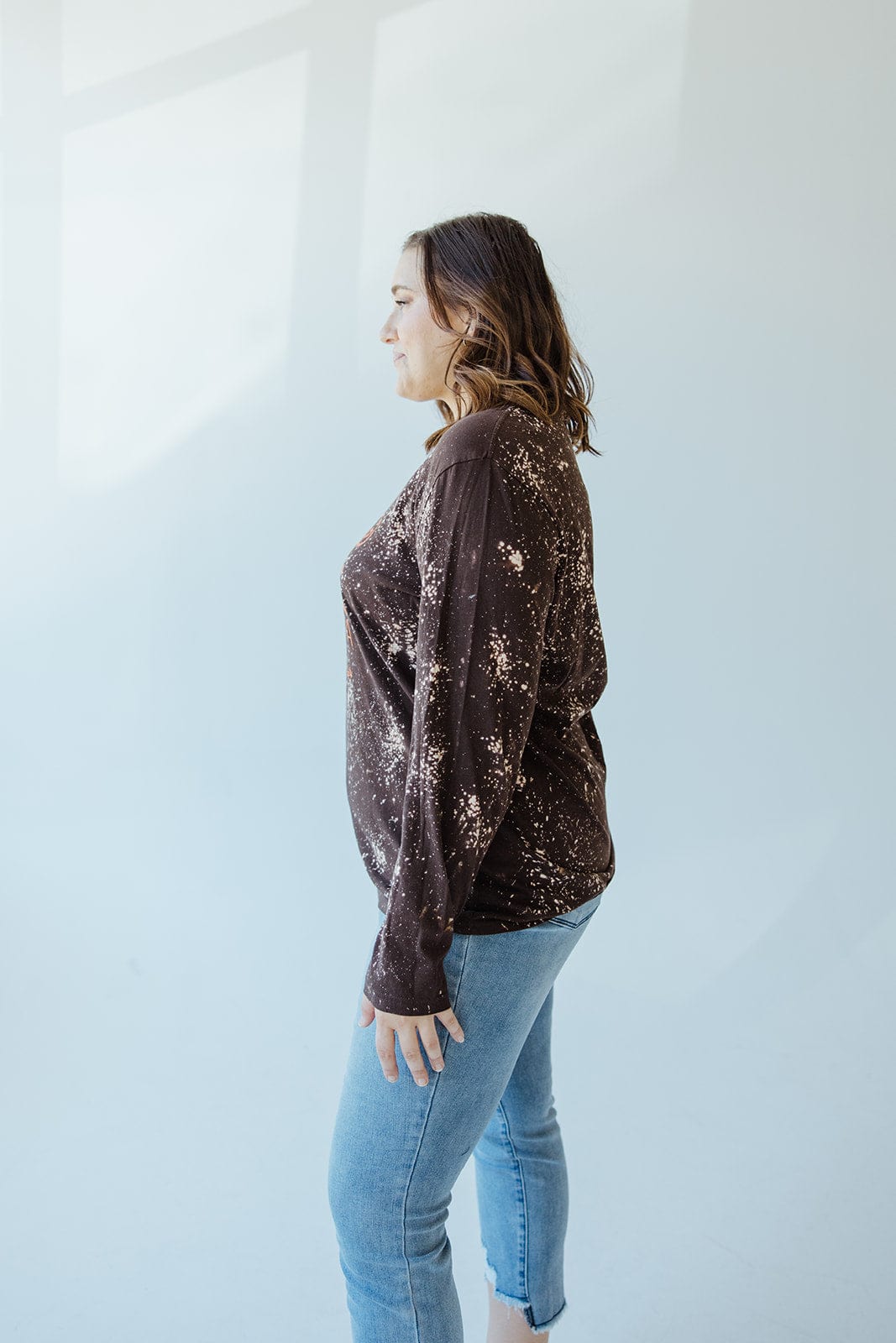 A woman stands in profile against a light background, wearing the "I LIKE MY ATTITUDE HOW I LIKE MY PUMPKINS WITH EXTRA SPICE" long-sleeve tee by Love Marlow and blue jeans.