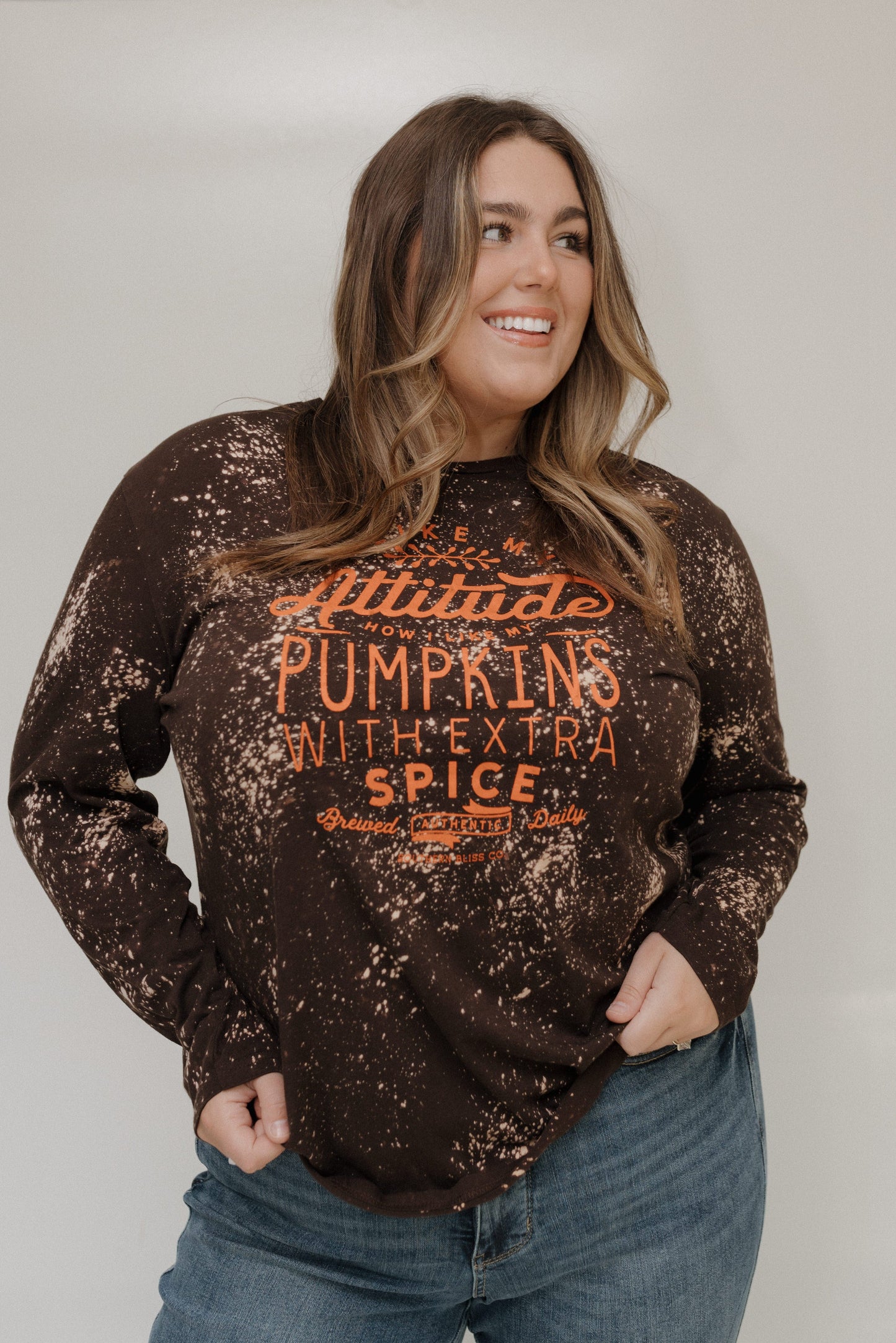 "I LIKE MY ATTITUDE HOW I LIKE MY PUMPKINS WITH EXTRA SPICE" LONG-SLEEVE TEE Love Marlow
Woman wearing a distressed brown sweatshirt with text, standing against a plain background