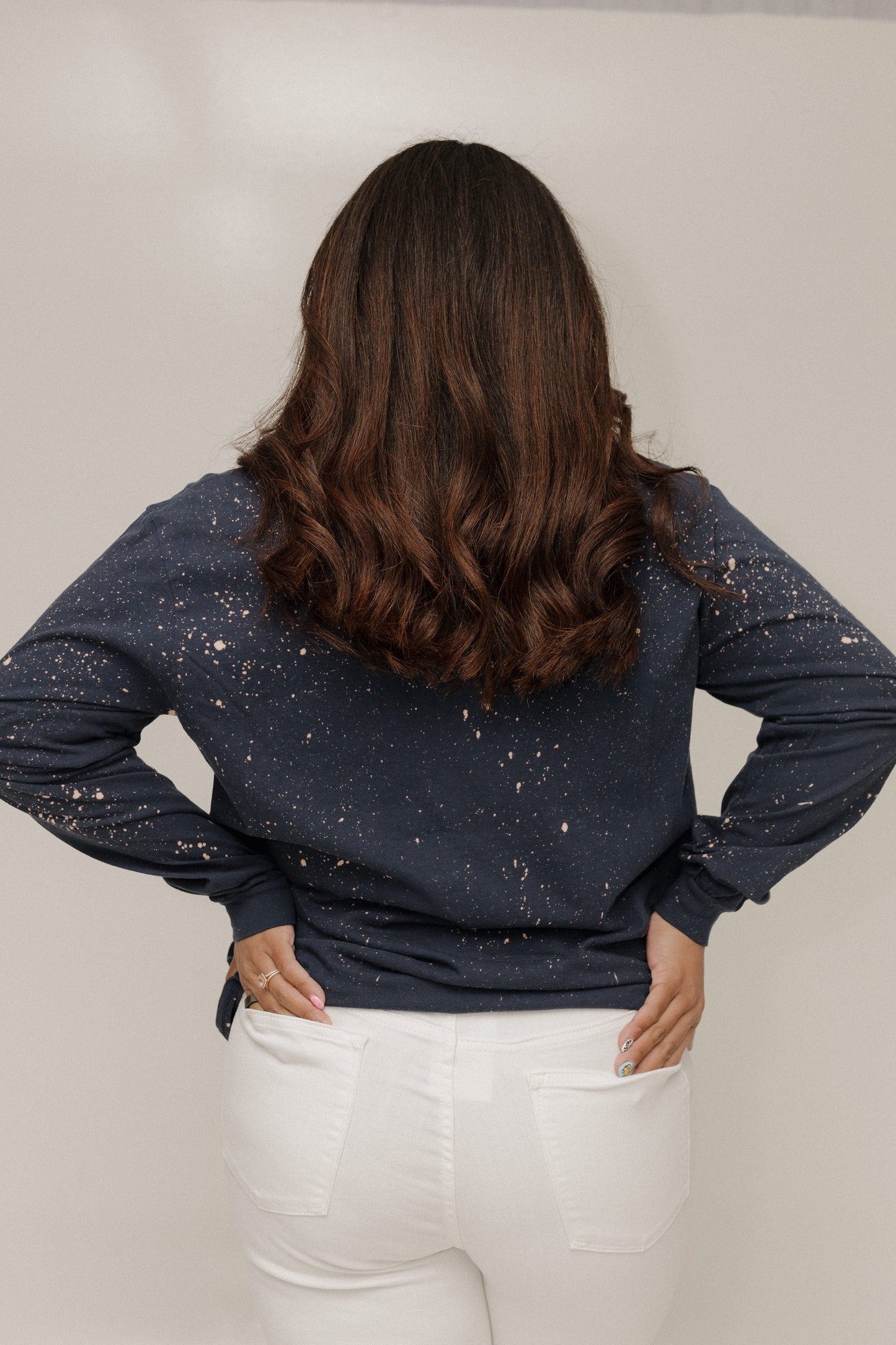 Person wearing a navy blue long-sleeve top with white speckles and white pants against a plain background