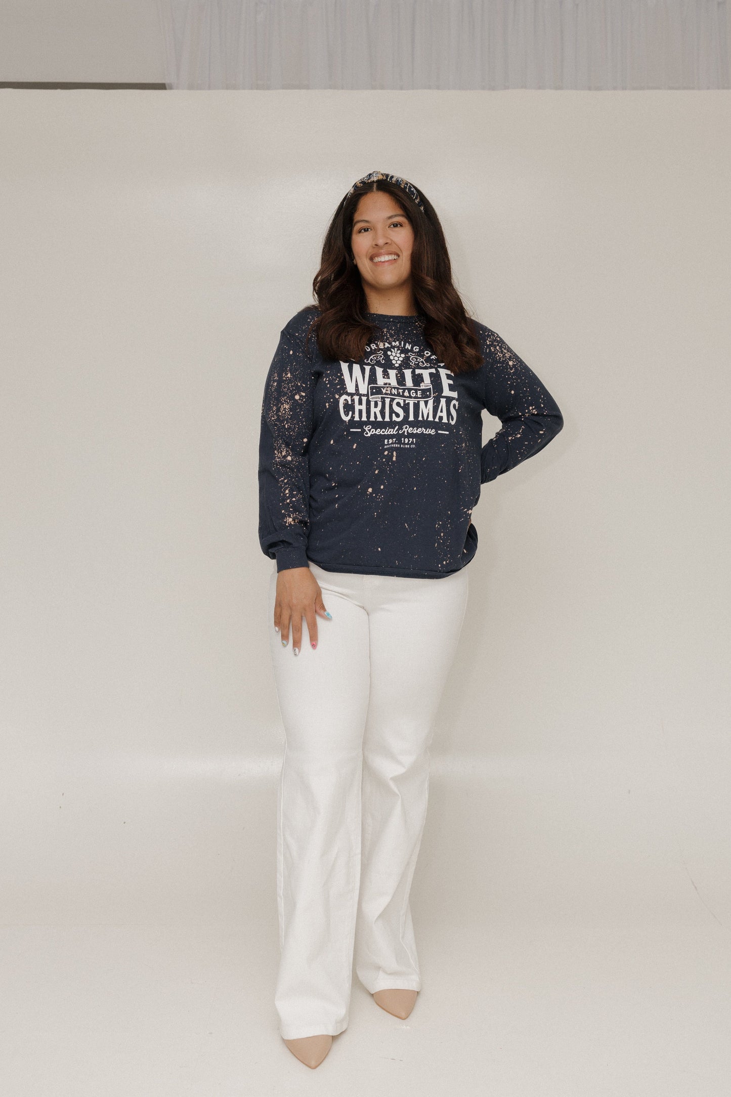 Person wearing a navy blue sweater with text and white pants on a plain background