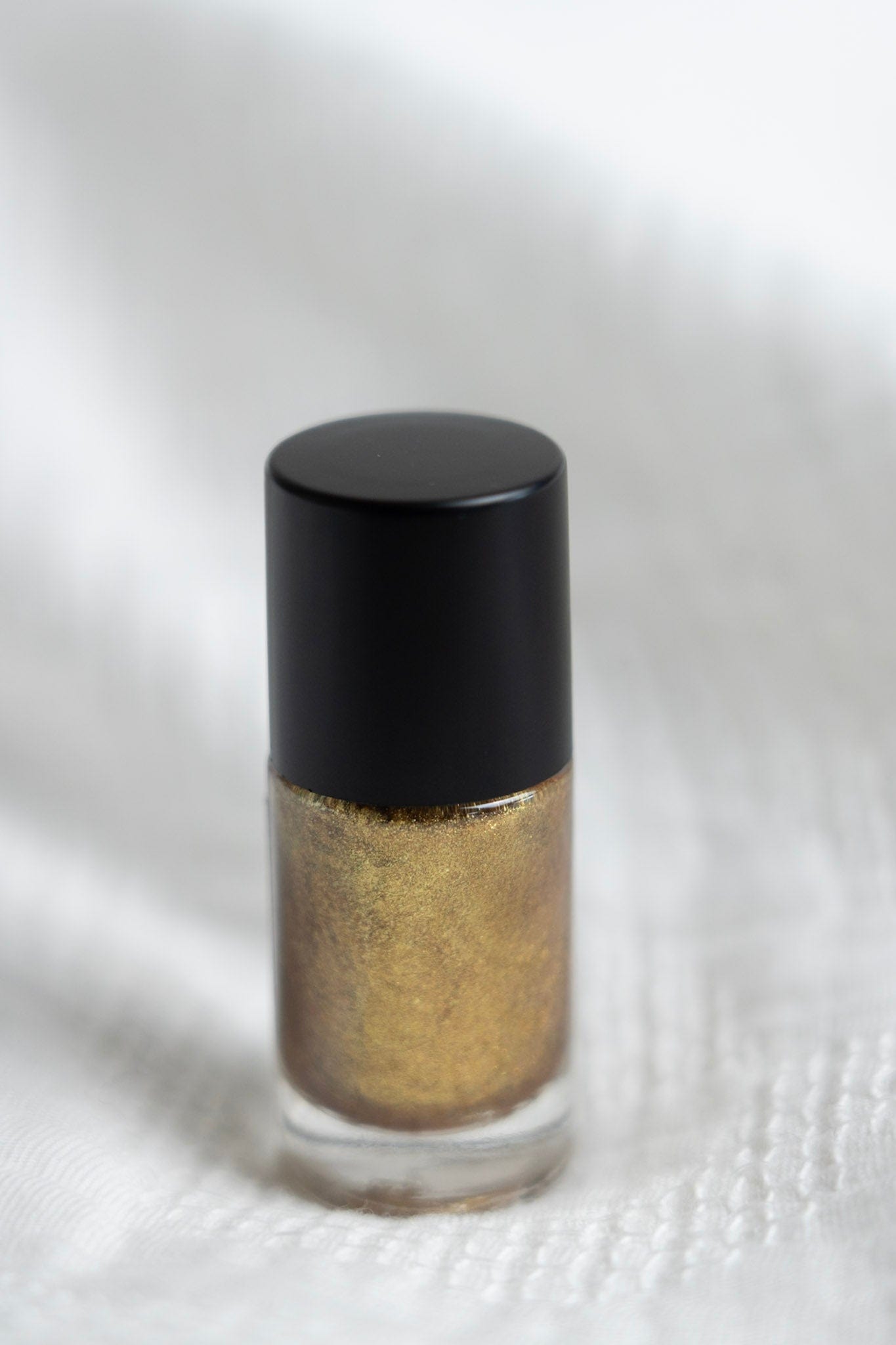 Gold nail polish with black cap on a white background