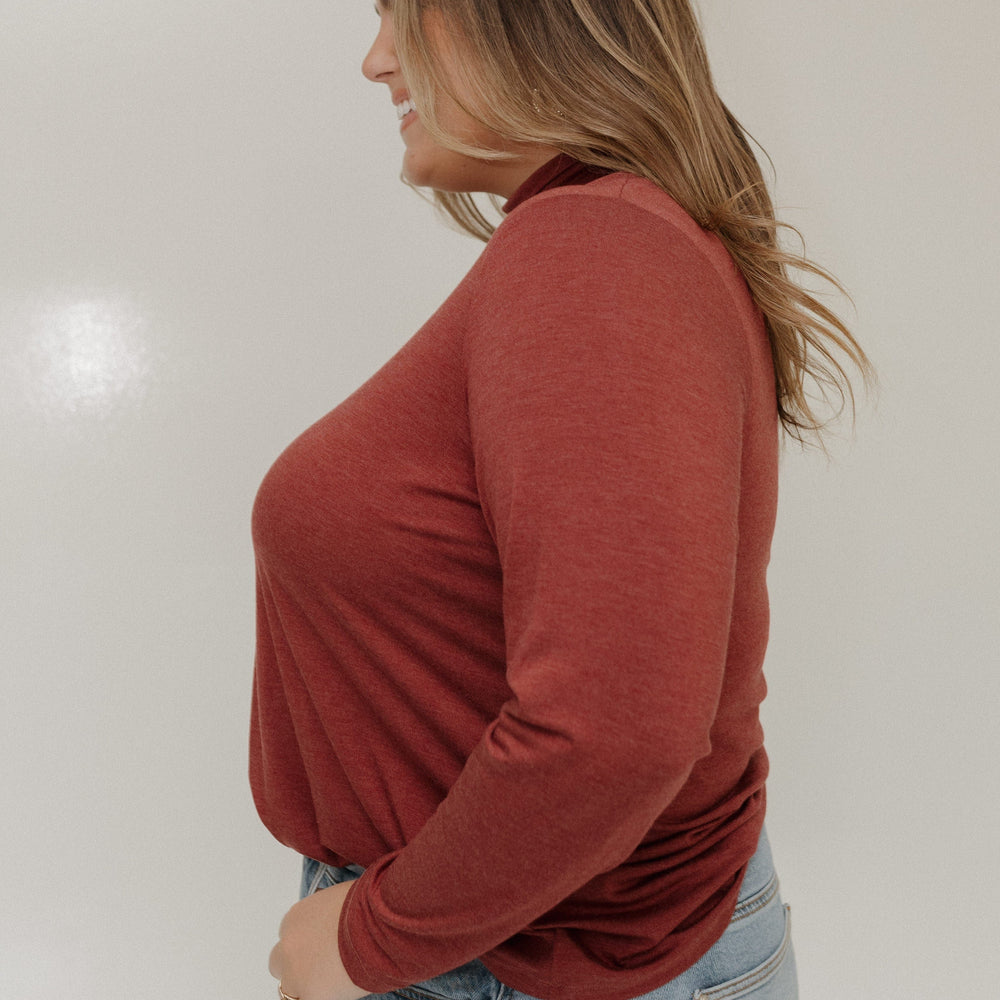Person wearing a rust-colored long-sleeve top and light blue jeans against a plain background