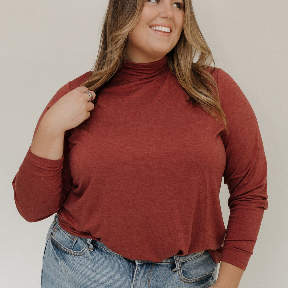 Woman wearing a rust-colored turtleneck and blue jeans against a plain background