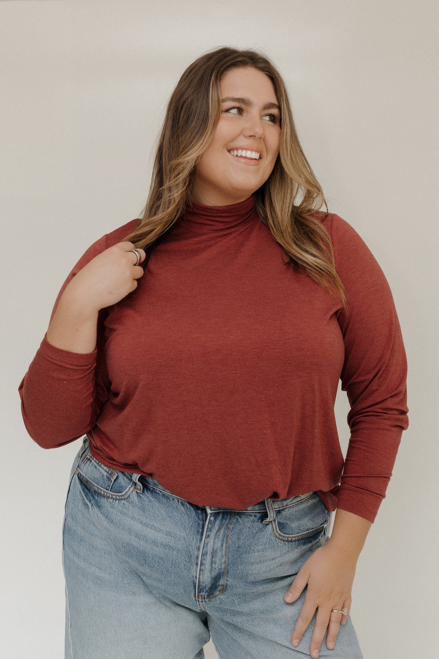 Woman wearing a rust-colored turtleneck and blue jeans against a plain background