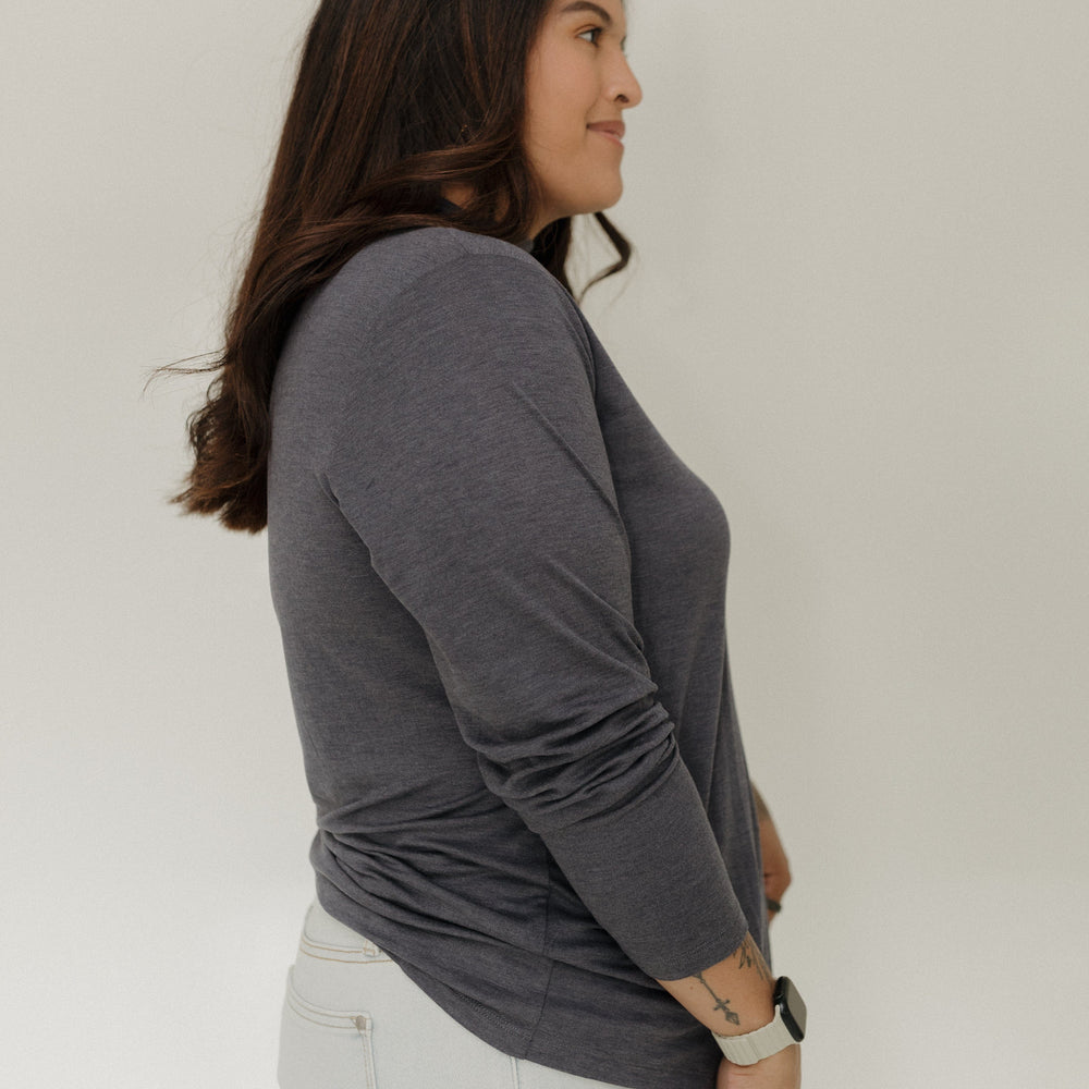 Woman wearing a gray long-sleeve top and white pants against a plain background
