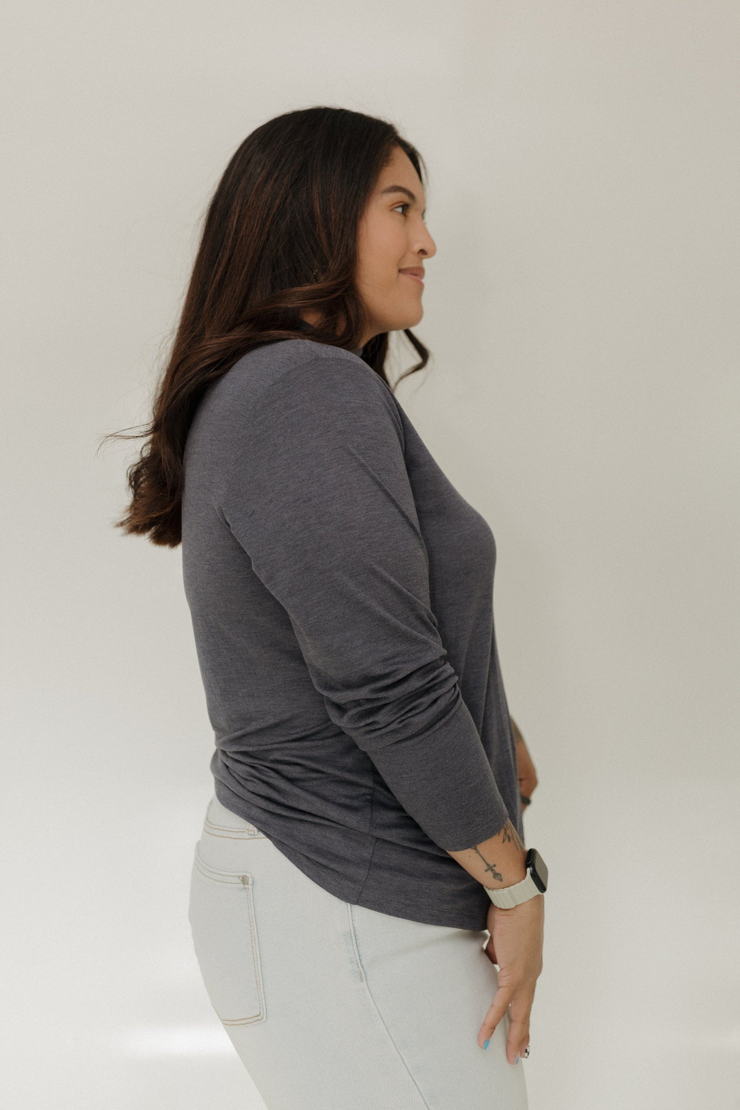 Woman wearing a gray long-sleeve top and white pants against a plain background