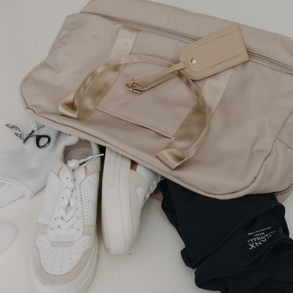 Beige bag, white sneakers, and black glasses on a light surface