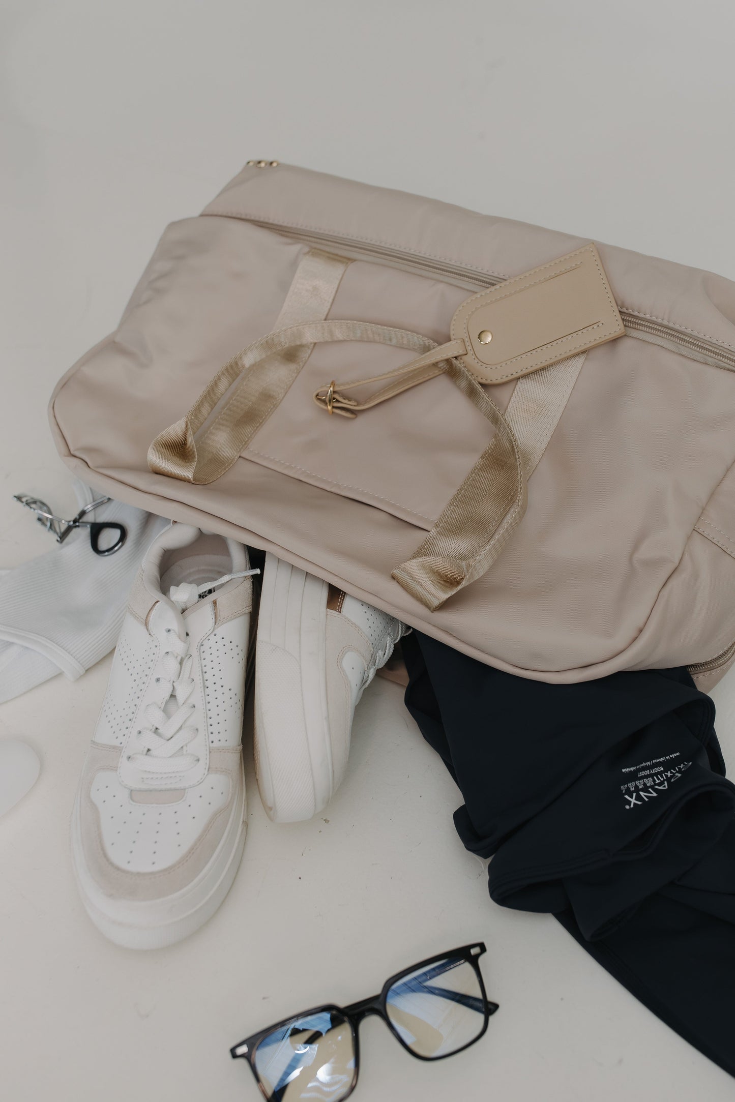 Beige bag, white sneakers, and black glasses on a light surface