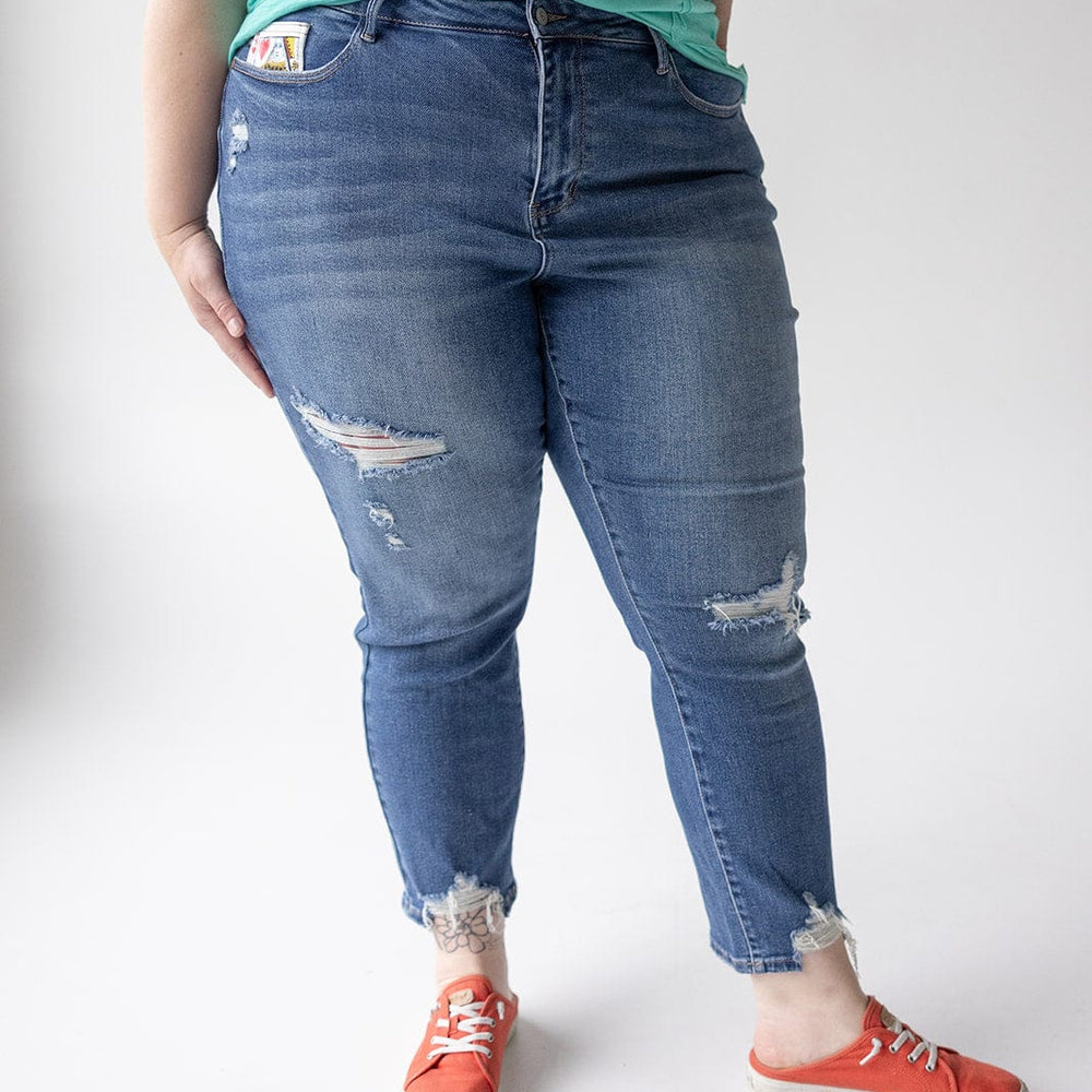 A person is standing wearing a green sleeveless top, distressed blue JUDY BLUE EMBROIDERED DESTROYED BOYFRIEND JEANS by Judy Blue, and red sneakers. Only the torso and legs are visible.