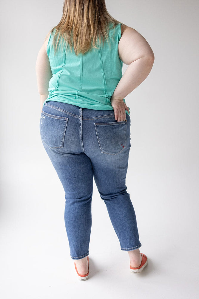 A person stands facing away from the camera, wearing a green sleeveless top, JUDY BLUE EMBROIDERED DESTROYED BOYFRIEND JEANS by Judy Blue, and red sandals.