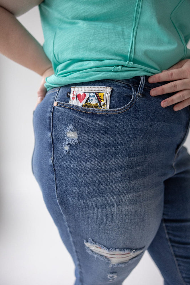 A person wearing a green top and Judy Blue JUDY BLUE EMBROIDERED DESTROYED BOYFRIEND JEANS with a playing card featuring the Queen of Hearts visible in the front pocket.