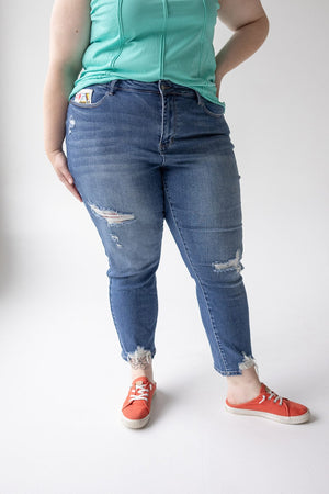 A person is standing wearing a green sleeveless top, distressed blue JUDY BLUE EMBROIDERED DESTROYED BOYFRIEND JEANS by Judy Blue, and red sneakers. Only the torso and legs are visible.