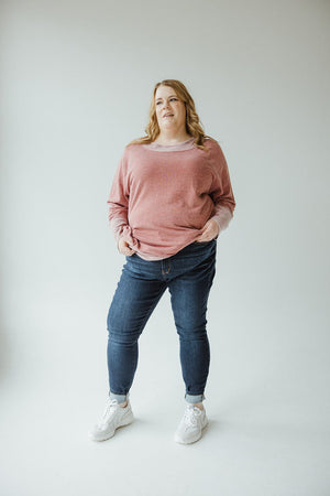 A person is standing against a plain background wearing a red long-sleeved shirt, Judy Blue High-Waisted Non-Distressed Skinny Jeans in Dark Wash, and white sneakers. Their hands are in their pockets, and they are looking slightly away from the camera.