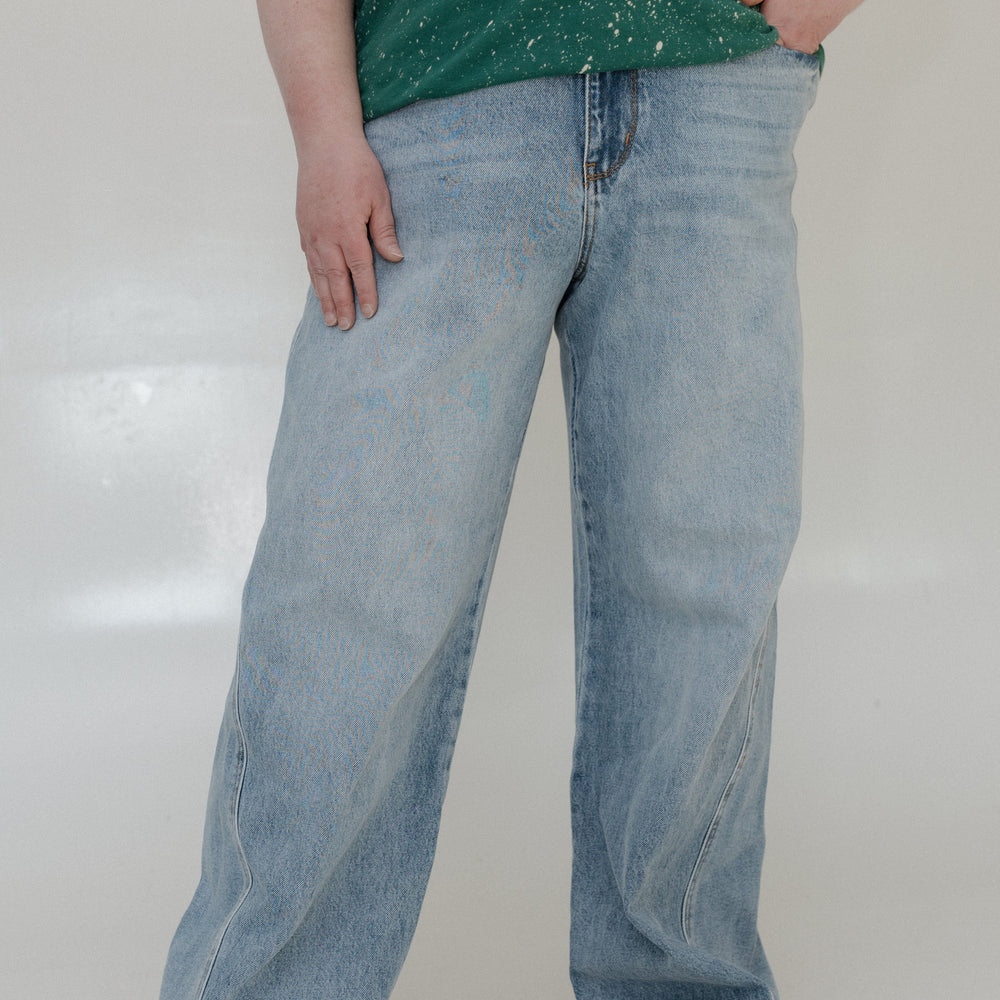 Person wearing a green splatter-painted shirt and light blue jeans on a white background