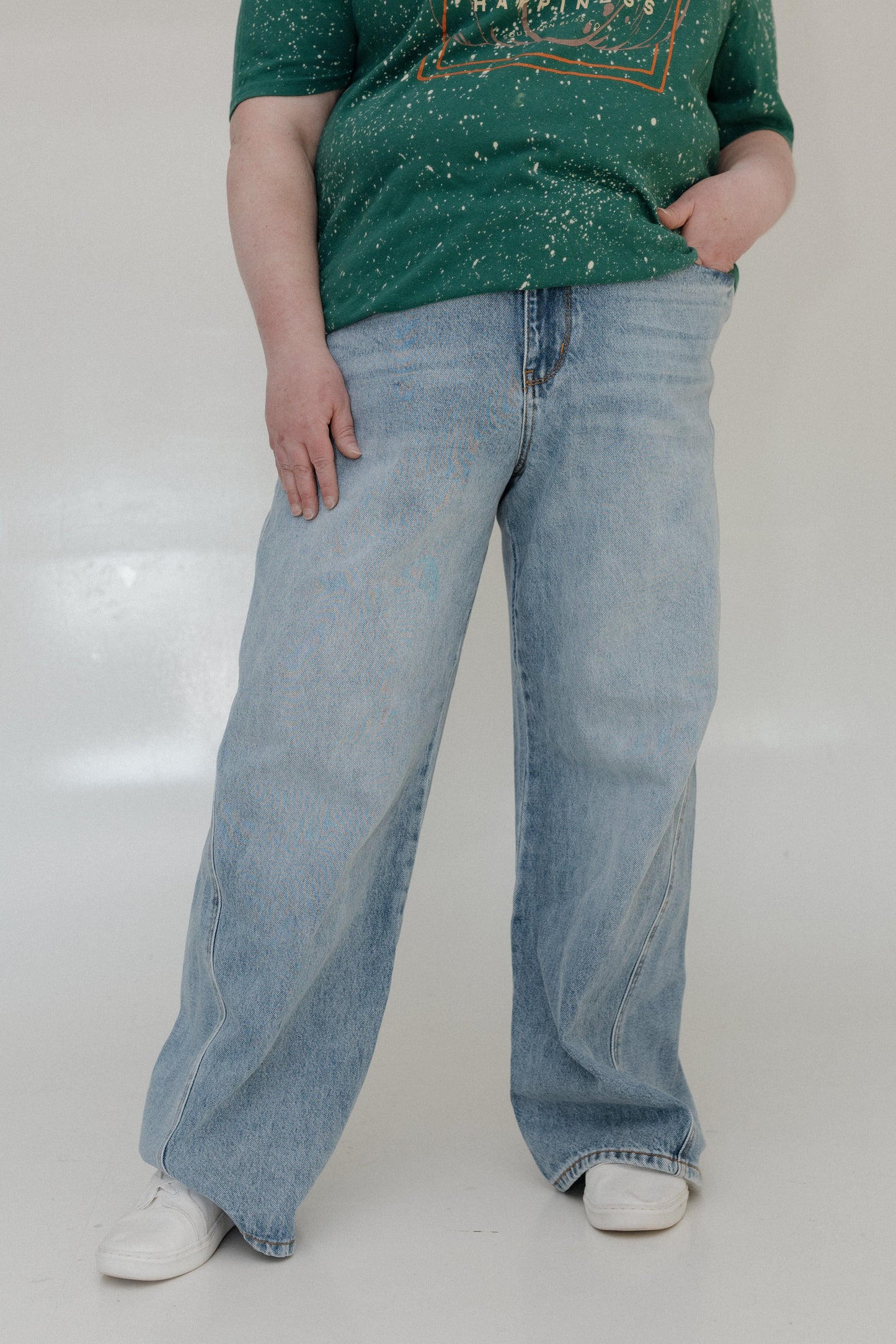 Person wearing a green splatter-painted shirt and light blue jeans on a white background