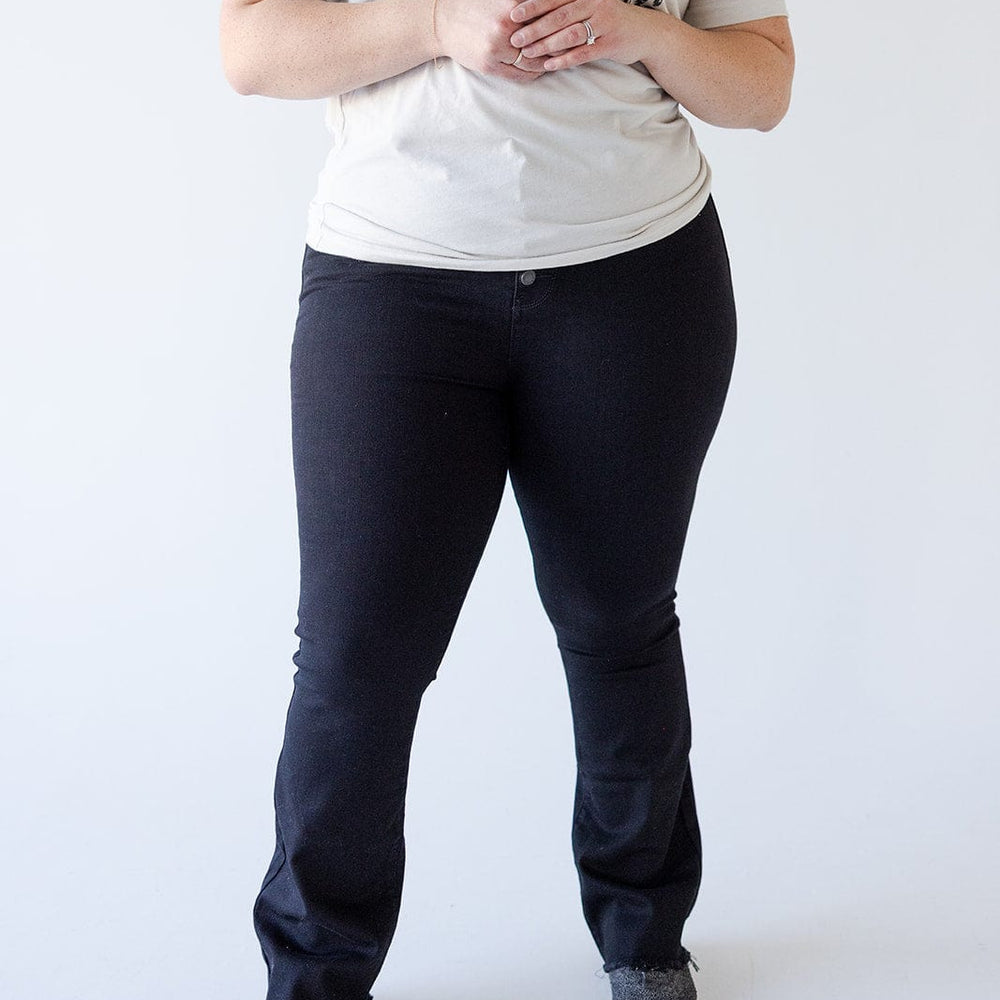 Person standing against a plain white background wearing a butterfly-patterned T-shirt, high waist jeans that accentuate their silhouette, and gray shoes.