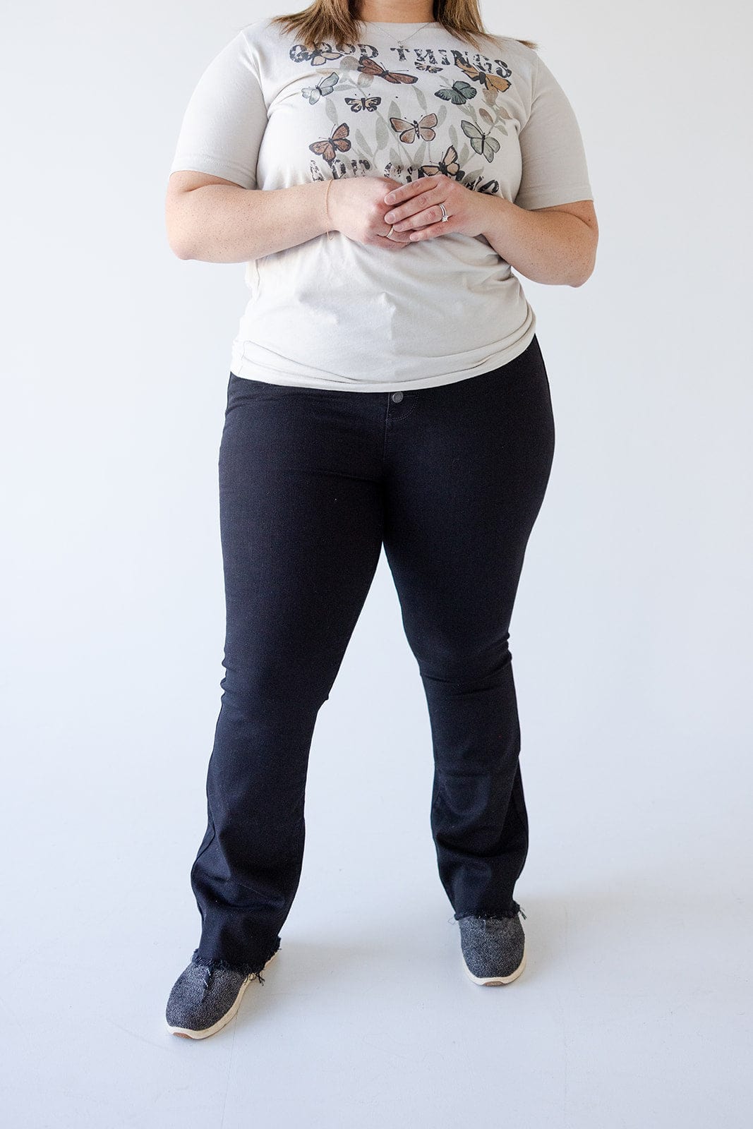 Person standing against a plain white background wearing a butterfly-patterned T-shirt, high waist jeans that accentuate their silhouette, and gray shoes.