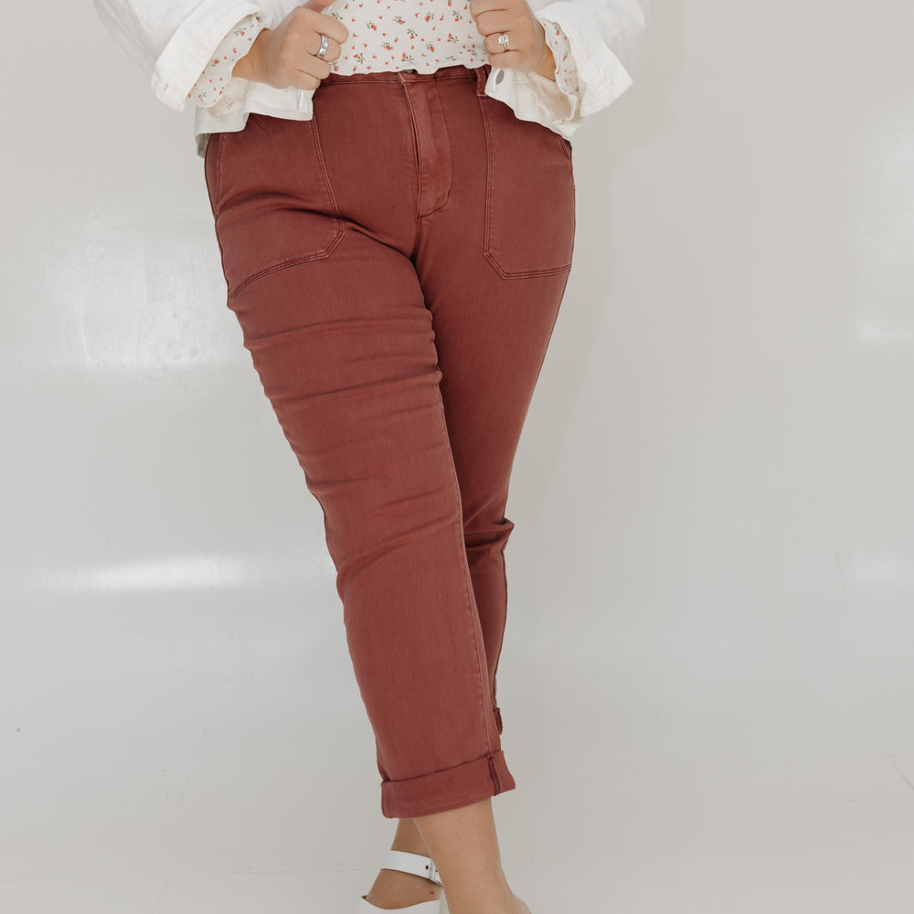 Person wearing a white jacket, patterned top, rust-colored pants, and white shoes on a light gray background